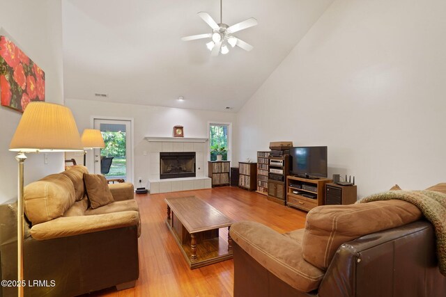 living area featuring high vaulted ceiling, a tiled fireplace, light wood-style floors, and ceiling fan