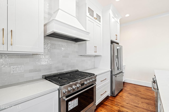 kitchen featuring crown molding, stainless steel appliances, decorative backsplash, white cabinets, and premium range hood