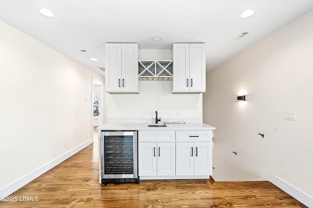 bar featuring wine cooler, a sink, visible vents, light wood-style floors, and indoor wet bar