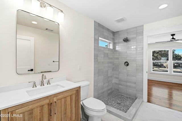 bathroom with toilet, vanity, a tile shower, and visible vents