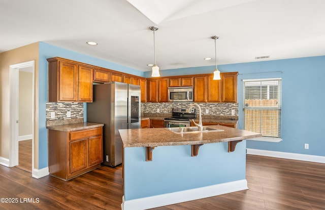 kitchen with pendant lighting, sink, a kitchen island with sink, stainless steel appliances, and a kitchen breakfast bar