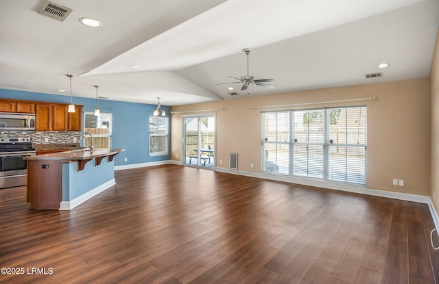 kitchen with vaulted ceiling, appliances with stainless steel finishes, a breakfast bar, pendant lighting, and decorative backsplash