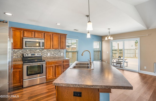 kitchen featuring sink, appliances with stainless steel finishes, a kitchen island with sink, hanging light fixtures, and decorative backsplash