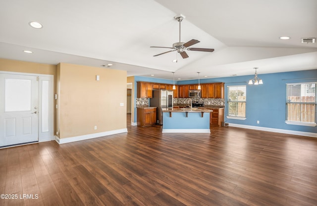 kitchen with decorative light fixtures, a center island with sink, dark hardwood / wood-style floors, stainless steel appliances, and backsplash