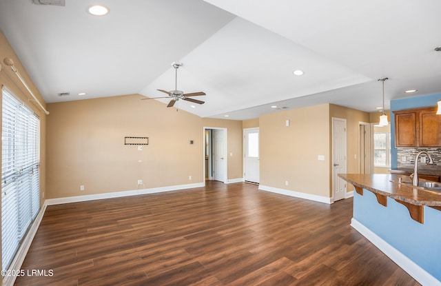 unfurnished living room featuring vaulted ceiling, dark hardwood / wood-style floors, sink, and a wealth of natural light