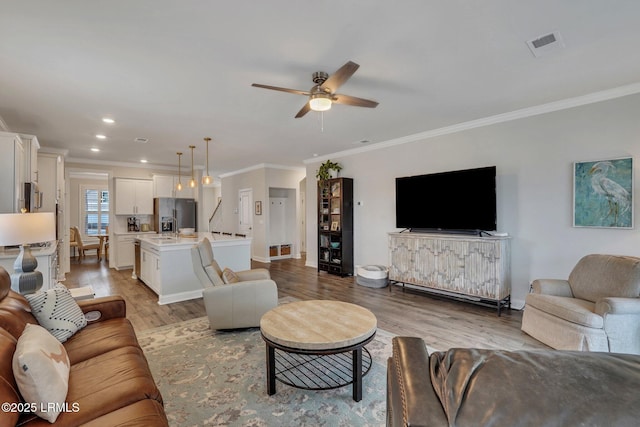 living area featuring light wood finished floors, visible vents, and ornamental molding