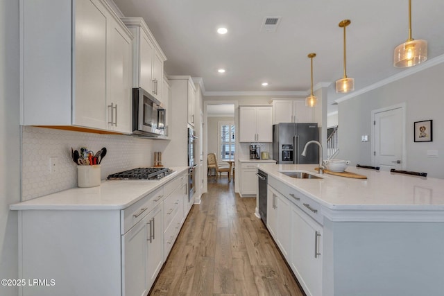 kitchen featuring a sink, white cabinets, ornamental molding, appliances with stainless steel finishes, and light wood-type flooring