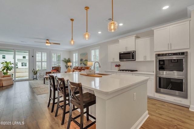 kitchen featuring stainless steel appliances, open floor plan, crown molding, and light wood-style flooring