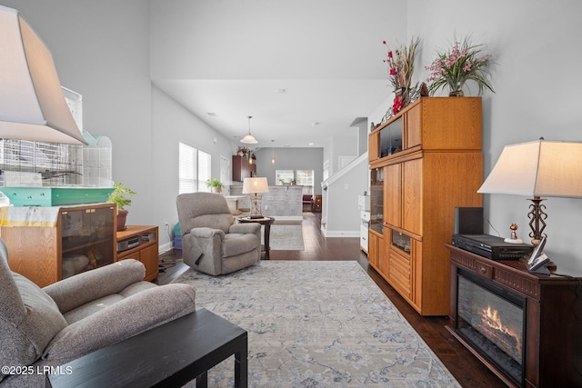 living room with dark wood-style floors, a glass covered fireplace, and baseboards