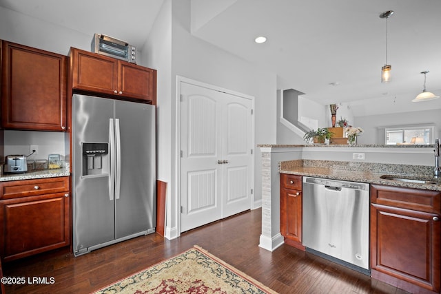 kitchen with dark wood-style floors, stainless steel appliances, hanging light fixtures, a sink, and light stone countertops