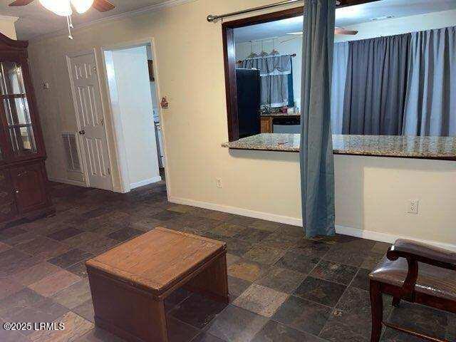 living area featuring crown molding, baseboards, a ceiling fan, and stone finish flooring