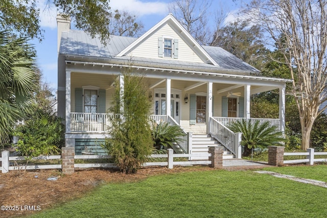 farmhouse-style home featuring a front lawn, a standing seam roof, a porch, fence, and metal roof