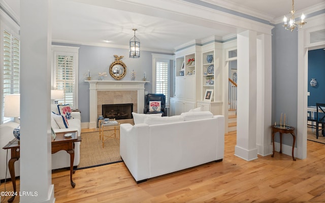 living room featuring a premium fireplace, ornamental molding, a notable chandelier, and light hardwood / wood-style floors