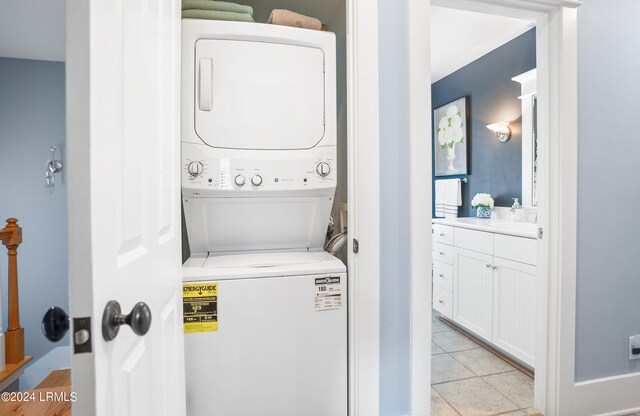 laundry area featuring stacked washing maching and dryer, sink, and light tile patterned floors