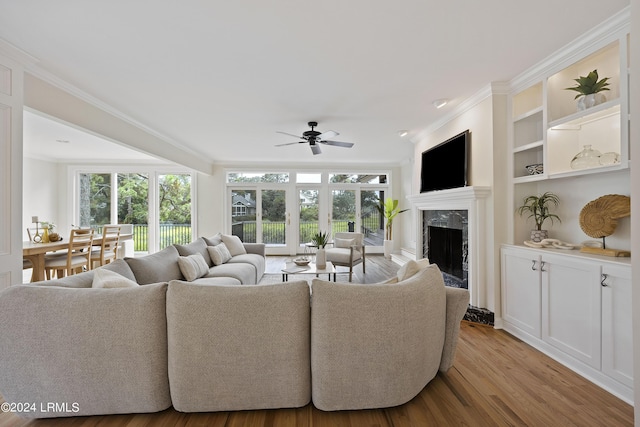 living room featuring a fireplace, ornamental molding, ceiling fan, light wood-type flooring, and built in shelves