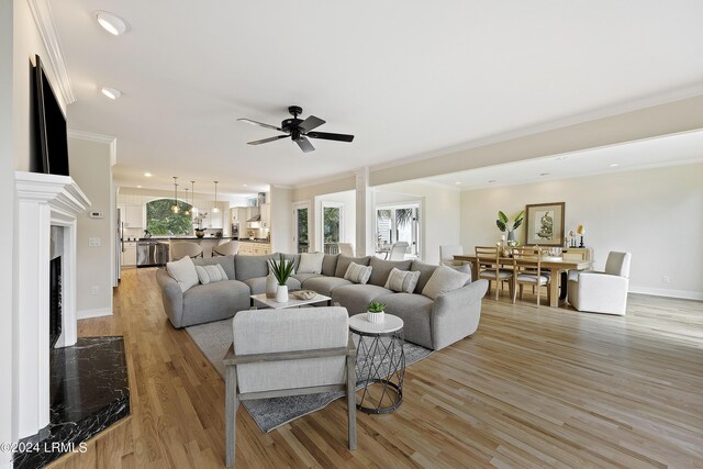 living room with ornamental molding, ceiling fan, a fireplace, and light hardwood / wood-style floors