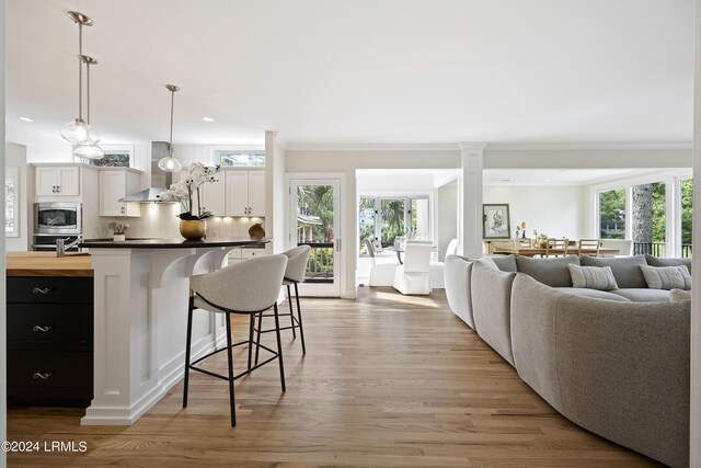 kitchen with ornate columns, a kitchen breakfast bar, pendant lighting, stainless steel appliances, and white cabinets