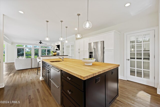 kitchen with high quality fridge, decorative light fixtures, white cabinetry, an island with sink, and butcher block counters