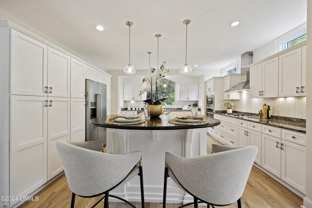 kitchen featuring wall chimney exhaust hood, hanging light fixtures, a kitchen island, stainless steel appliances, and decorative backsplash