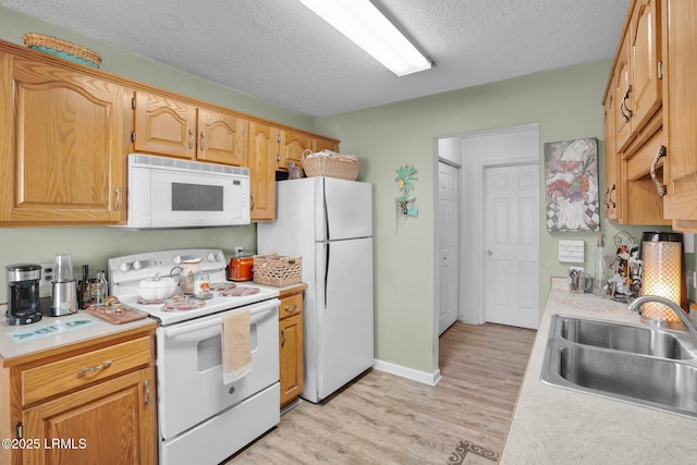 kitchen with sink, white appliances, a textured ceiling, and light wood-type flooring