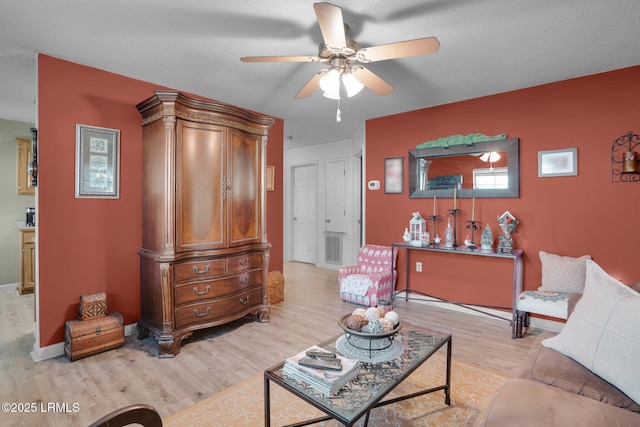 living room with ceiling fan, a textured ceiling, and light wood-type flooring