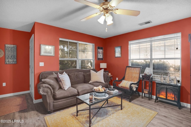 living room featuring ceiling fan, hardwood / wood-style flooring, a textured ceiling, and a wood stove