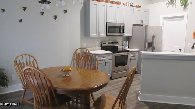 kitchen with dark wood-type flooring, baseboards, stainless steel appliances, and light countertops