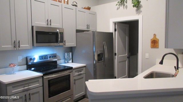 kitchen featuring appliances with stainless steel finishes, light countertops, a sink, and gray cabinetry