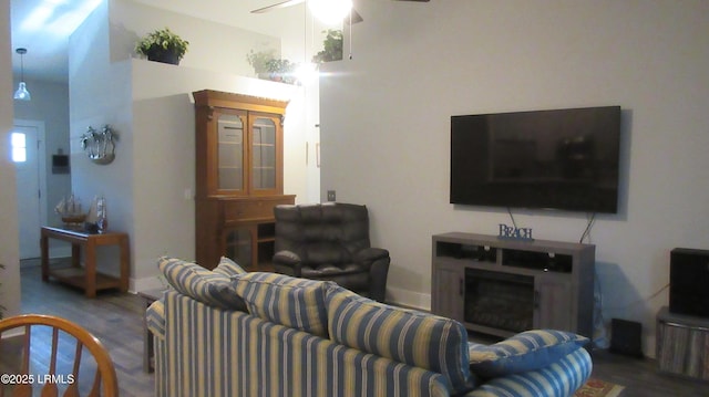 living area featuring a high ceiling, a fireplace, wood finished floors, a ceiling fan, and baseboards