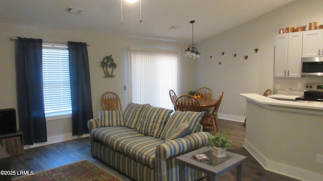 living room featuring dark wood-style floors, baseboards, visible vents, and a notable chandelier