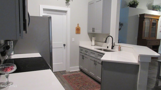 kitchen featuring electric range oven, dark wood-style floors, a peninsula, light countertops, and a sink