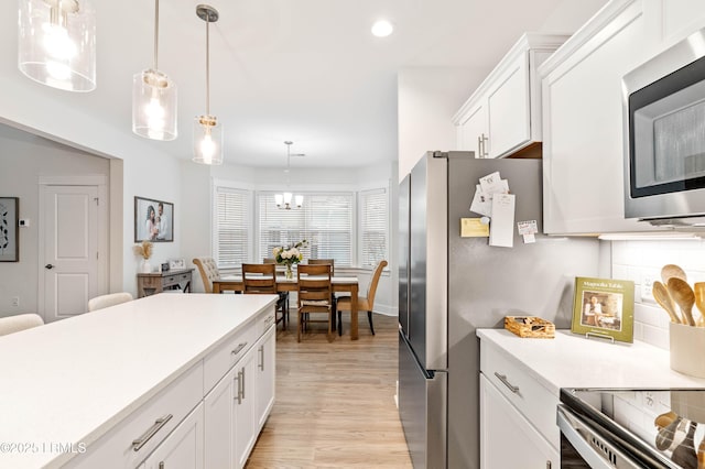 kitchen with white cabinets, light countertops, light wood finished floors, stainless steel microwave, and pendant lighting