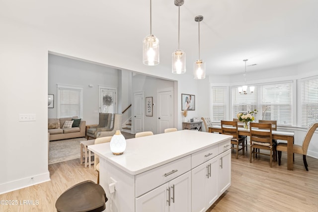 kitchen with white cabinets, a center island, light countertops, light wood-type flooring, and pendant lighting