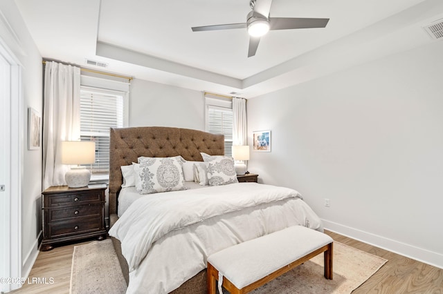 bedroom with light wood-style floors, a raised ceiling, visible vents, and baseboards