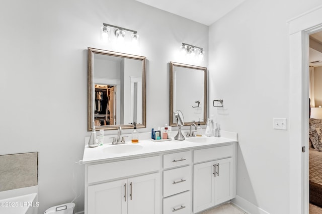 full bathroom with baseboards, double vanity, a sink, and connected bathroom