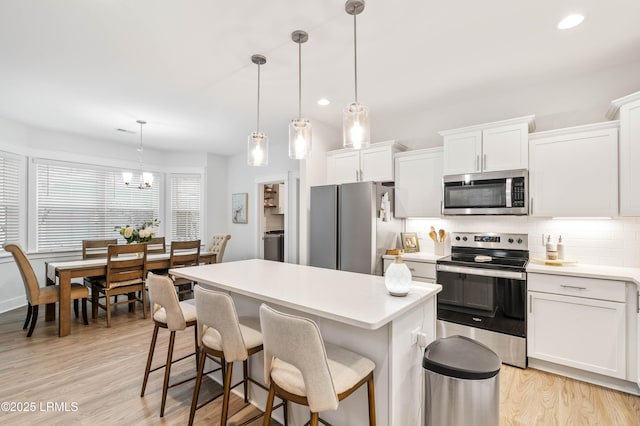 kitchen featuring a center island, stainless steel appliances, light wood-type flooring, white cabinetry, and backsplash