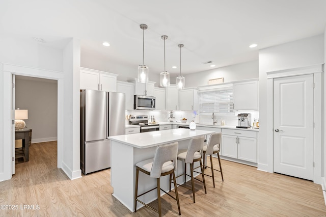 kitchen with appliances with stainless steel finishes, light wood-type flooring, a sink, and a breakfast bar