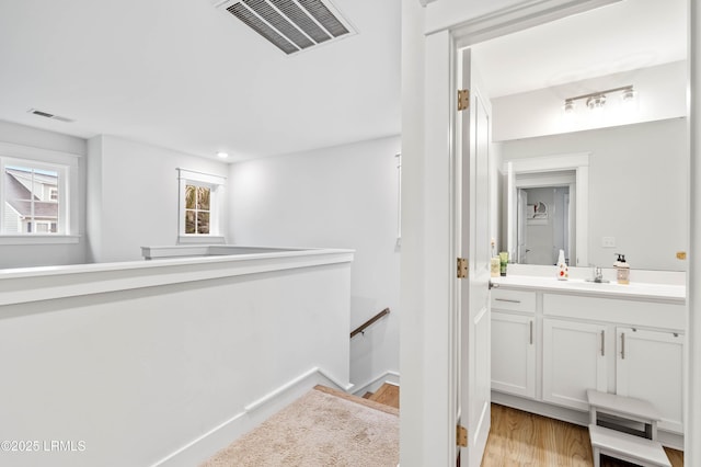 hall with visible vents, a sink, light wood finished floors, and an upstairs landing