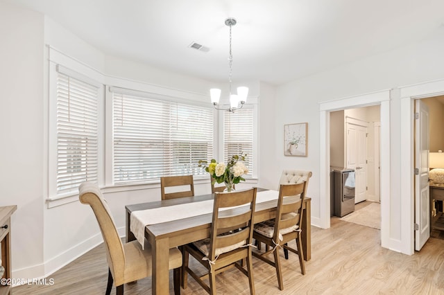 dining space featuring washer / dryer, light wood-type flooring, a chandelier, and visible vents