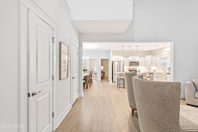 hall with baseboards, a sink, and light wood-style floors