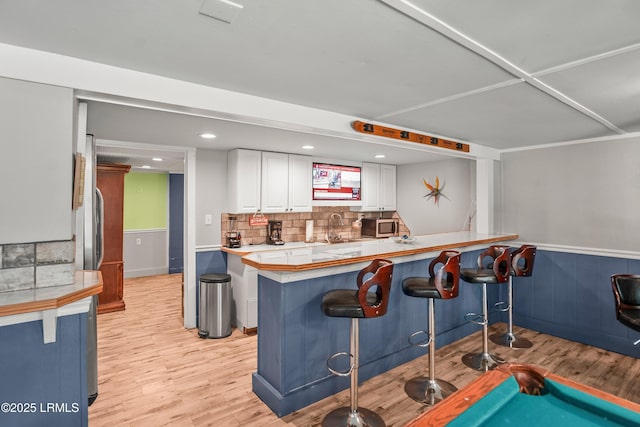 373 Pike Dr, Fripp Island, SC 29920 - kitchen with stainless steel microwave, a kitchen breakfast bar, white cabinets, light wood-type flooring, and a wainscoted wall