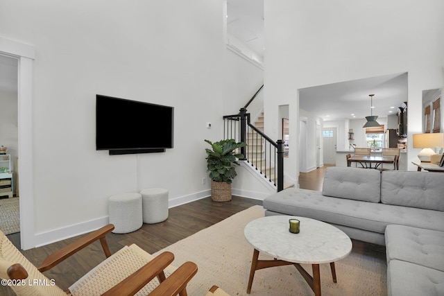 living area with stairs, wood finished floors, a towering ceiling, and baseboards
