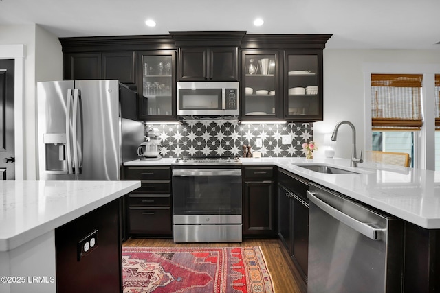 kitchen with a sink, light wood finished floors, a peninsula, stainless steel appliances, and decorative backsplash