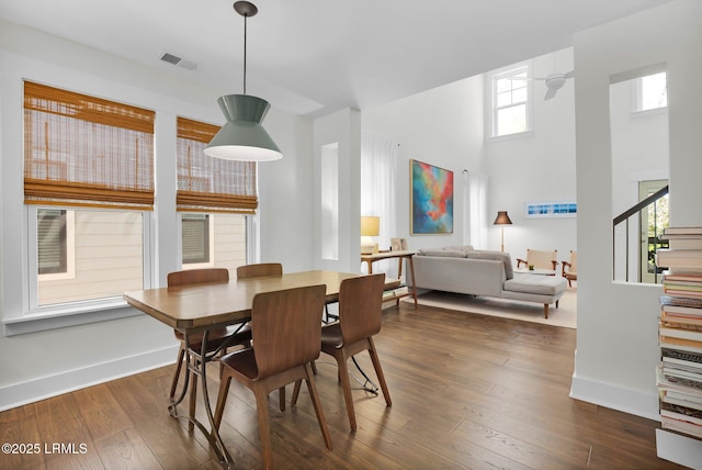 dining area with stairway, dark wood-type flooring, baseboards, a towering ceiling, and visible vents