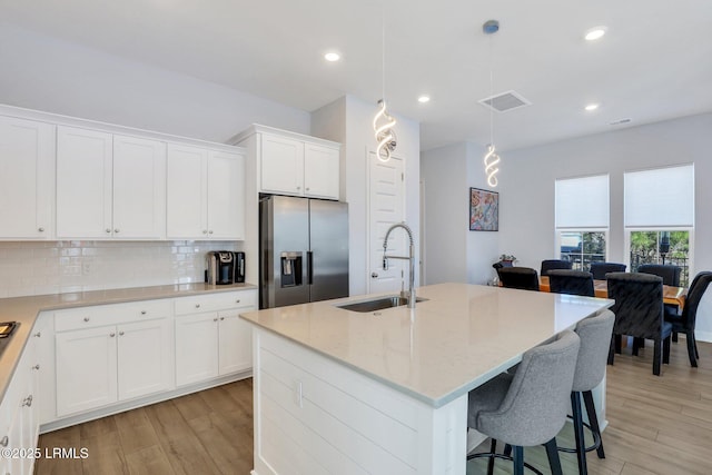 kitchen featuring light wood-style flooring, light stone countertops, a sink, stainless steel refrigerator with ice dispenser, and decorative backsplash