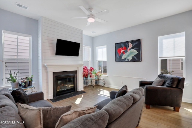 living room with a large fireplace, baseboards, visible vents, and wood finished floors
