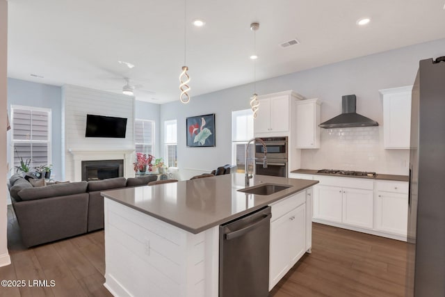 kitchen featuring a large fireplace, visible vents, appliances with stainless steel finishes, open floor plan, and wall chimney range hood