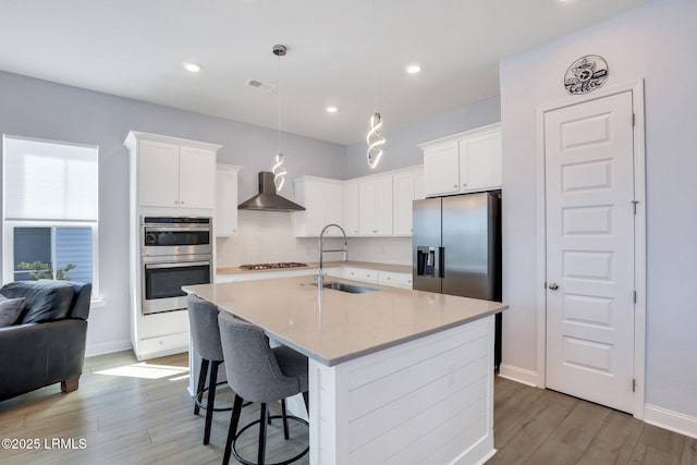 kitchen with light wood-style flooring, stainless steel appliances, a sink, white cabinetry, and wall chimney exhaust hood