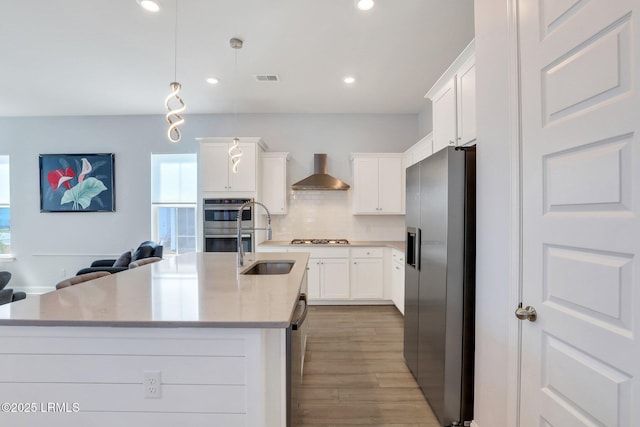 kitchen featuring backsplash, light wood-style flooring, appliances with stainless steel finishes, open floor plan, and wall chimney range hood