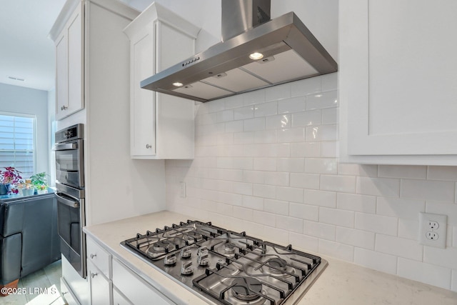 kitchen with wall chimney exhaust hood, appliances with stainless steel finishes, white cabinets, and tasteful backsplash
